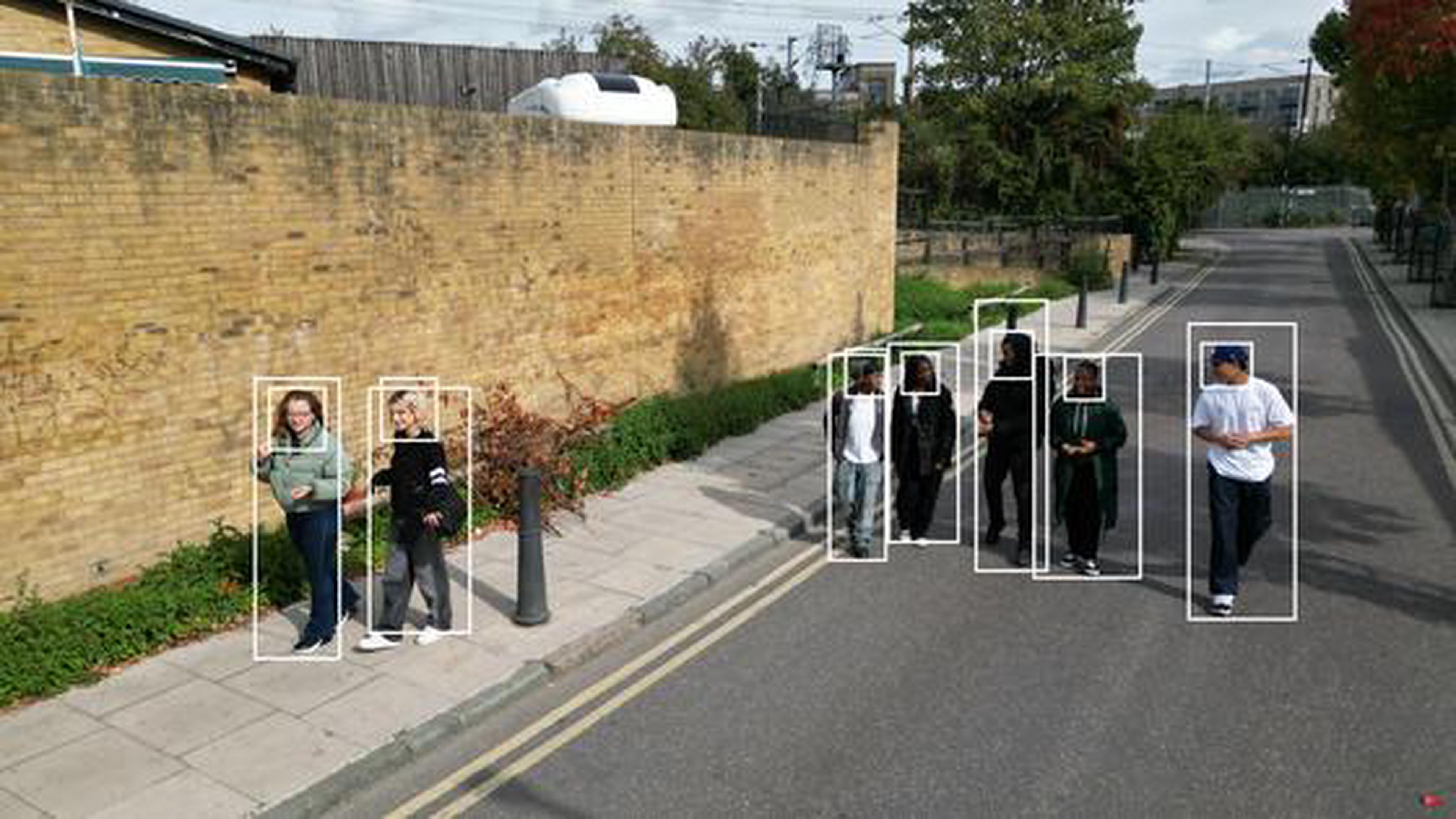 Young adults are walking on a street. Two young women are on the pavement to the left of the image and five young men walk in the road. The road is empty of traffic and the people in the picture are relaxed and appear to be engaged in chatting with each other. Overlaid on the image are identification boxes. All of the figures have ID boxes around them.